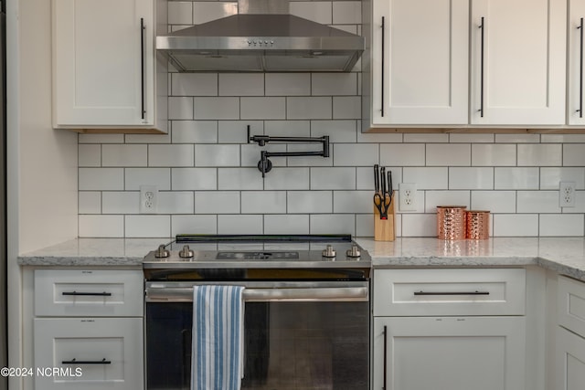 kitchen with stainless steel range oven, white cabinets, and wall chimney range hood