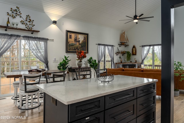 kitchen featuring light stone counters, light hardwood / wood-style floors, lofted ceiling, ceiling fan, and a kitchen island