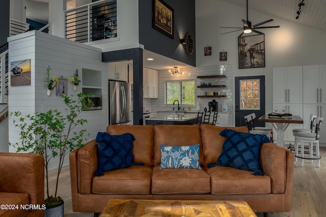 living room featuring light wood-type flooring, high vaulted ceiling, sink, and ceiling fan