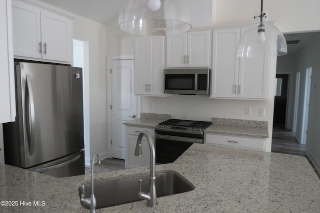 kitchen with sink, appliances with stainless steel finishes, hanging light fixtures, light stone counters, and white cabinets