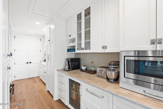 kitchen featuring white cabinetry, stainless steel microwave, light wood-type flooring, wine cooler, and light stone counters