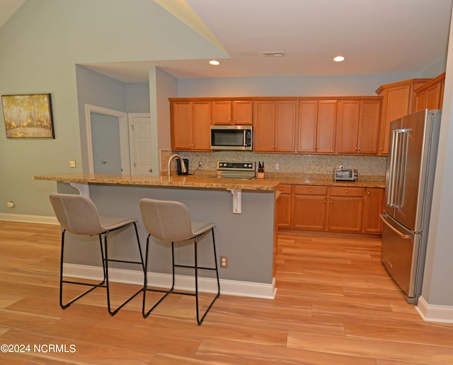 kitchen with appliances with stainless steel finishes, backsplash, and light wood-type flooring