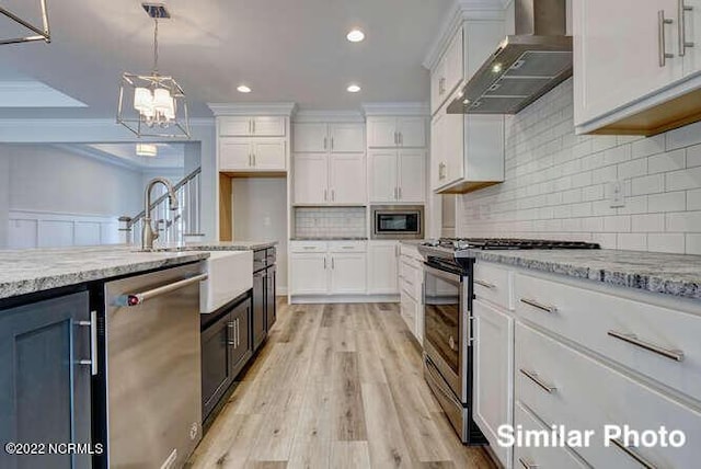 kitchen featuring hanging light fixtures, appliances with stainless steel finishes, ornamental molding, white cabinets, and wall chimney exhaust hood