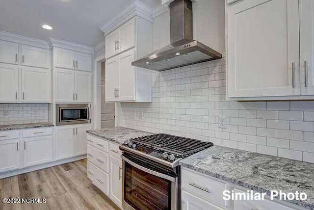 kitchen with white cabinetry, light wood-style floors, wall chimney range hood, appliances with stainless steel finishes, and light stone countertops