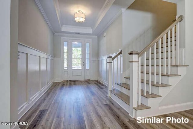 foyer entrance with a decorative wall, wood finished floors, ornamental molding, wainscoting, and a tray ceiling