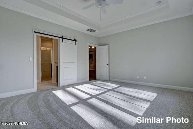 unfurnished bedroom featuring carpet floors, a tray ceiling, crown molding, and a barn door