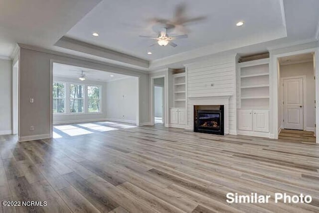 unfurnished living room featuring ornamental molding, a tray ceiling, a glass covered fireplace, and wood finished floors