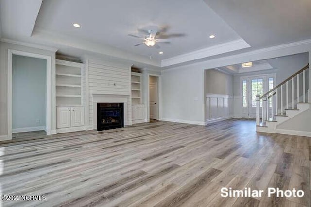 unfurnished living room with stairs, a tray ceiling, a fireplace, and crown molding