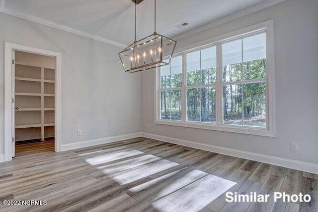 unfurnished dining area featuring baseboards, a chandelier, crown molding, and wood finished floors