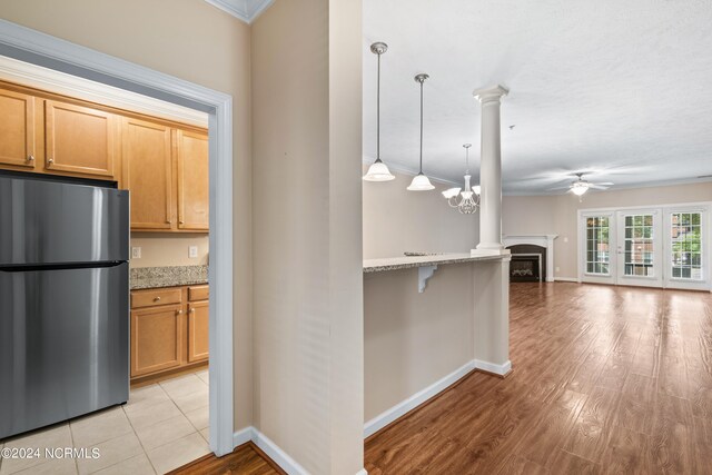 kitchen with a fireplace, ceiling fan with notable chandelier, crown molding, light wood-type flooring, and stainless steel fridge