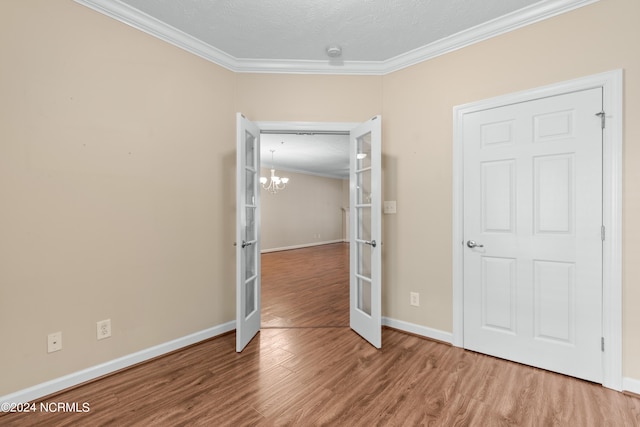 unfurnished bedroom with french doors, wood-type flooring, ornamental molding, and a notable chandelier