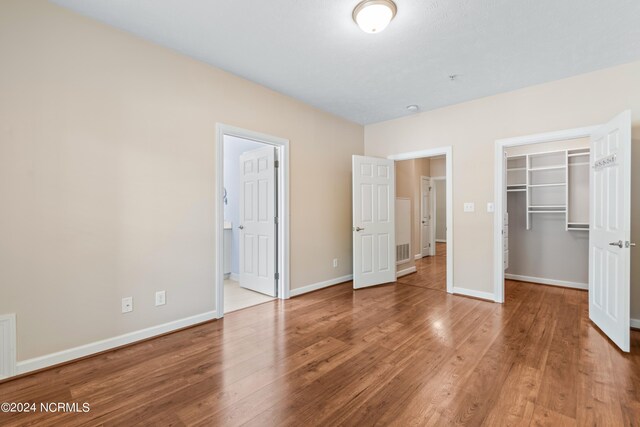 unfurnished bedroom with hardwood / wood-style flooring, a closet, ensuite bath, and a walk in closet