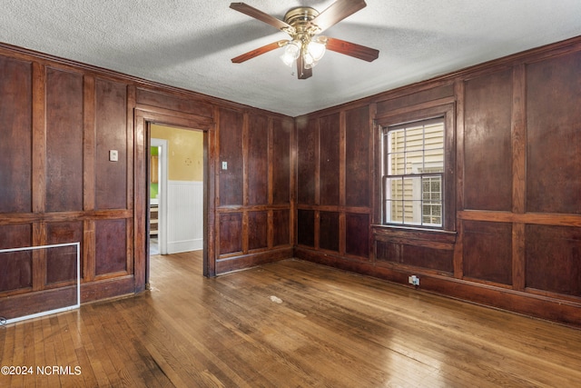 spare room featuring a textured ceiling, ceiling fan, wood walls, and dark hardwood / wood-style flooring