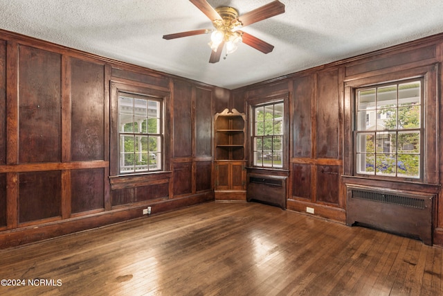 empty room featuring radiator, dark wood-type flooring, wood walls, and a textured ceiling