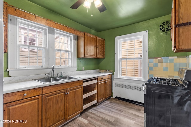 kitchen featuring light hardwood / wood-style flooring, sink, radiator heating unit, stainless steel gas range oven, and decorative backsplash