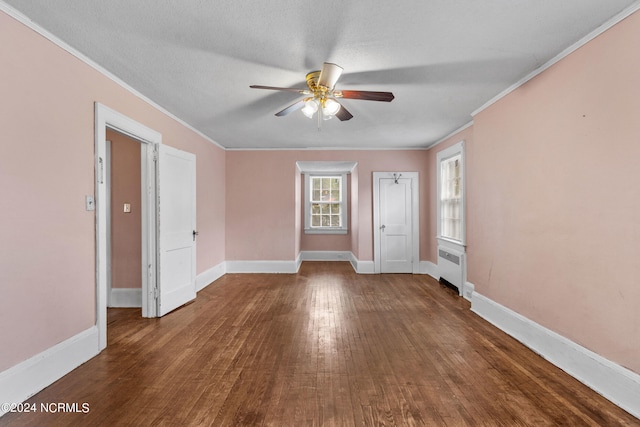 empty room with radiator, ornamental molding, ceiling fan, a textured ceiling, and dark wood-type flooring