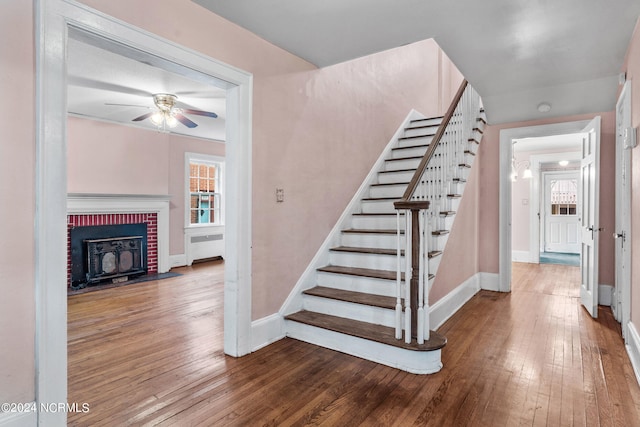 stairway with a brick fireplace, ceiling fan, radiator, and wood-type flooring