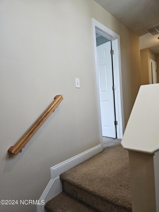 stairway featuring carpet floors and a textured ceiling