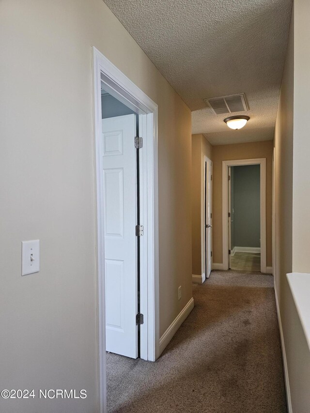 hall featuring carpet and a textured ceiling