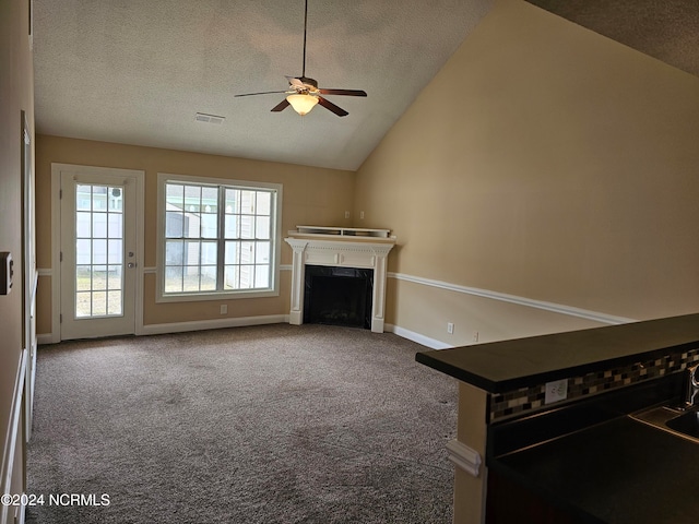 unfurnished living room featuring lofted ceiling, a textured ceiling, carpet, and ceiling fan