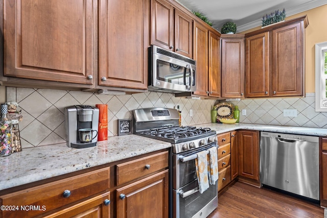 kitchen with appliances with stainless steel finishes, tasteful backsplash, light stone counters, ornamental molding, and dark wood-type flooring