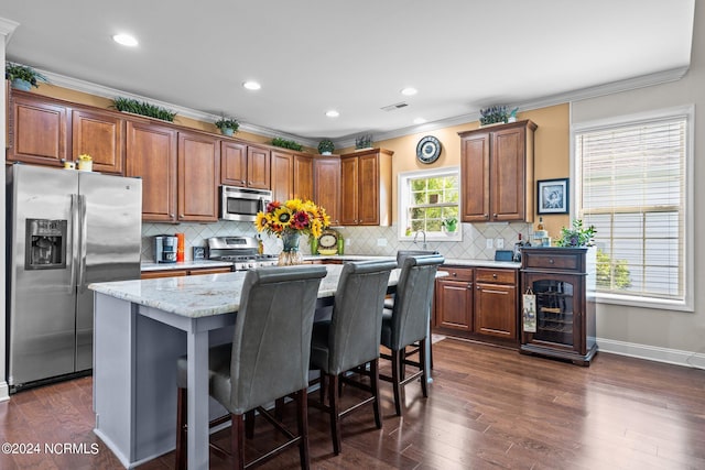 kitchen with appliances with stainless steel finishes, dark hardwood / wood-style flooring, backsplash, crown molding, and a center island