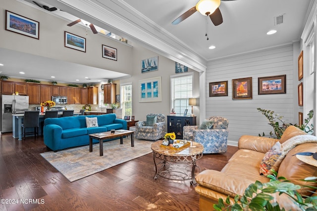 living room featuring ceiling fan, dark hardwood / wood-style flooring, wood walls, a towering ceiling, and ornamental molding