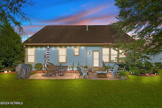 back house at dusk featuring a fire pit, a patio, and a lawn