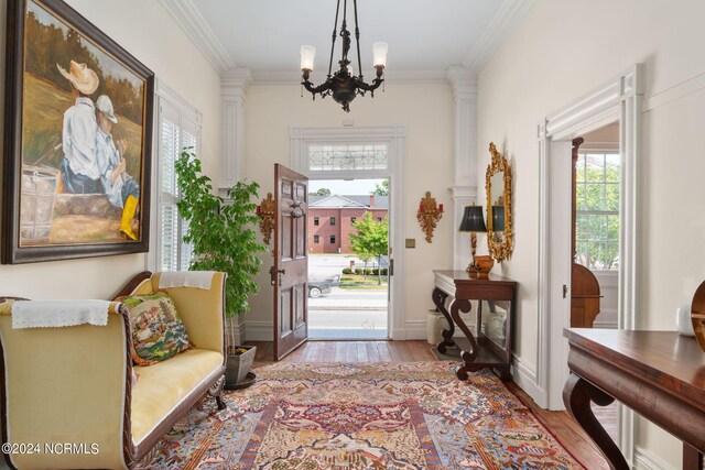 foyer entrance featuring a notable chandelier, ornate columns, light hardwood / wood-style flooring, and crown molding