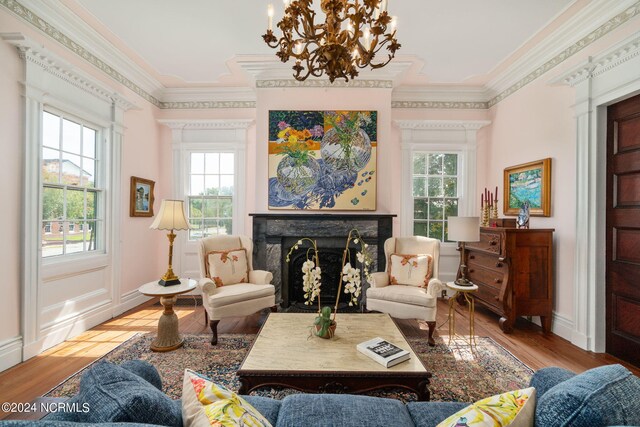 living room featuring a fireplace, a notable chandelier, crown molding, and light hardwood / wood-style flooring