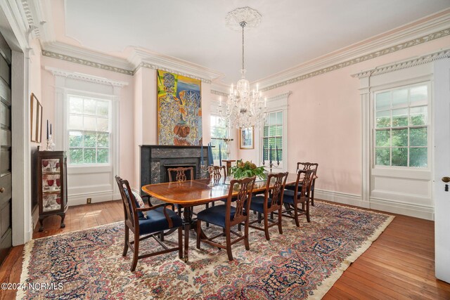 dining room with ornamental molding, an inviting chandelier, wood-type flooring, and a high end fireplace