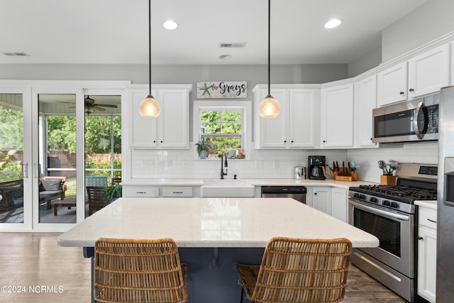 kitchen with sink, decorative light fixtures, a kitchen island, white cabinetry, and stainless steel appliances