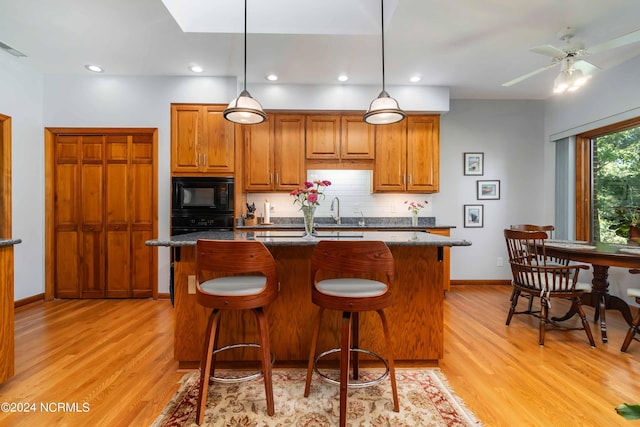 kitchen with a kitchen island with sink, tasteful backsplash, black appliances, and brown cabinets