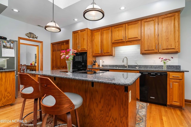 kitchen featuring tasteful backsplash, decorative light fixtures, a sink, light wood-style flooring, and black appliances