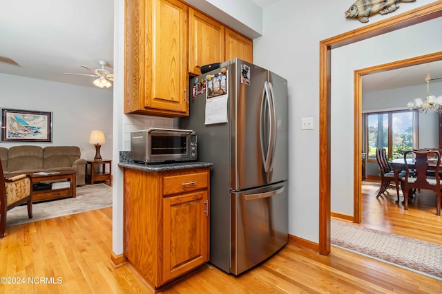 kitchen featuring brown cabinetry, light wood-style flooring, decorative backsplash, and freestanding refrigerator