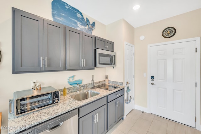 kitchen with gray cabinetry, stainless steel appliances, light stone countertops, light tile patterned floors, and sink