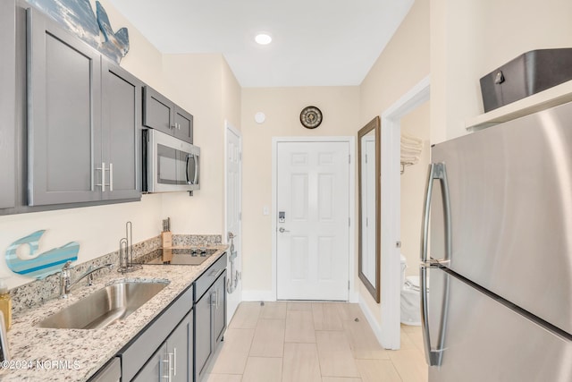 kitchen with appliances with stainless steel finishes, sink, light stone counters, and gray cabinetry