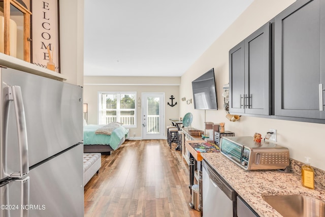 kitchen with gray cabinetry, light wood-type flooring, appliances with stainless steel finishes, and light stone counters