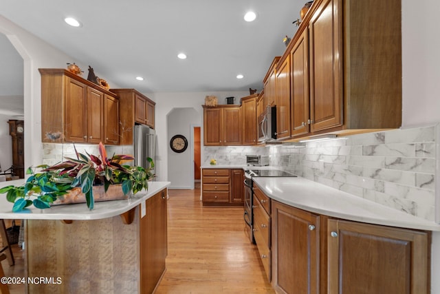 kitchen featuring appliances with stainless steel finishes, light wood-type flooring, tasteful backsplash, and a breakfast bar