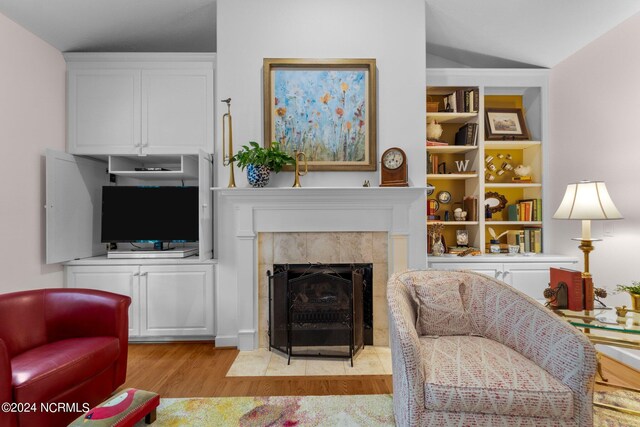 living room featuring a tile fireplace, light wood-type flooring, and vaulted ceiling