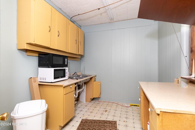 kitchen with white microwave, light countertops, light floors, black microwave, and a sink