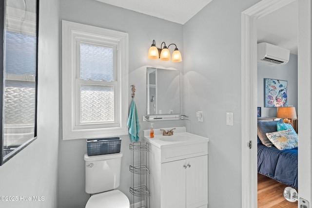 ensuite bathroom with an AC wall unit, toilet, ensuite bathroom, wood finished floors, and vanity