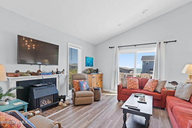 living room featuring lofted ceiling, a glass covered fireplace, and wood finished floors