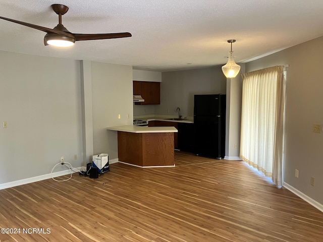 kitchen with a sink, under cabinet range hood, freestanding refrigerator, a peninsula, and light countertops