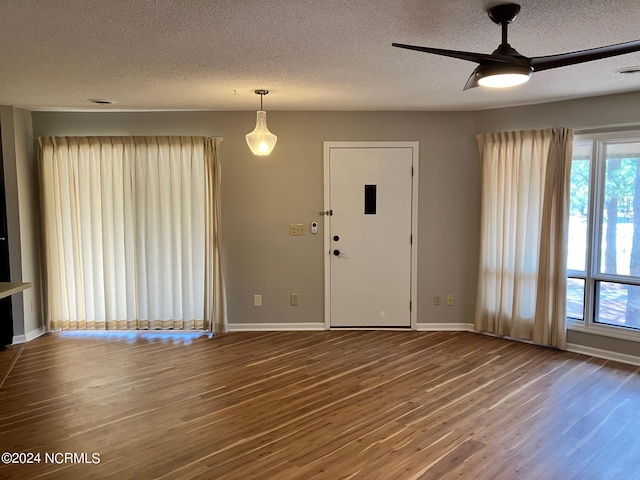 unfurnished living room featuring a wealth of natural light, baseboards, wood finished floors, and a ceiling fan