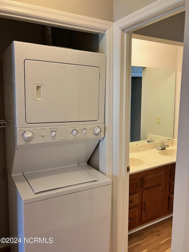 laundry room with laundry area, stacked washer / dryer, wood finished floors, and a sink