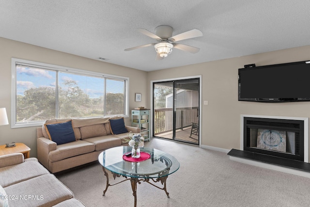 living area featuring a textured ceiling, a fireplace with raised hearth, visible vents, a ceiling fan, and carpet