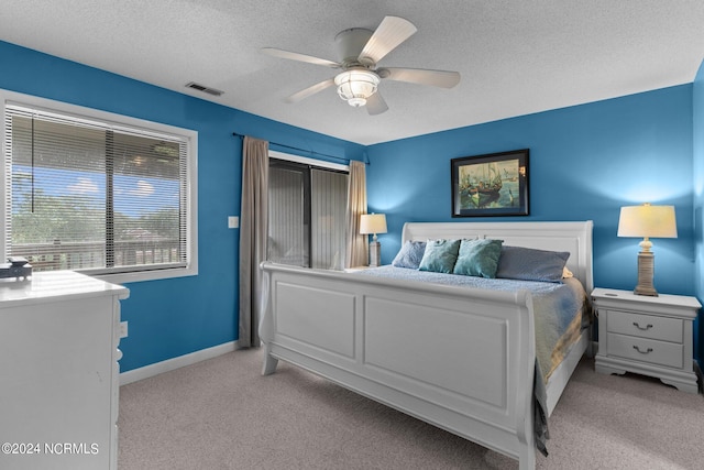 bedroom with light carpet, baseboards, visible vents, a ceiling fan, and a textured ceiling