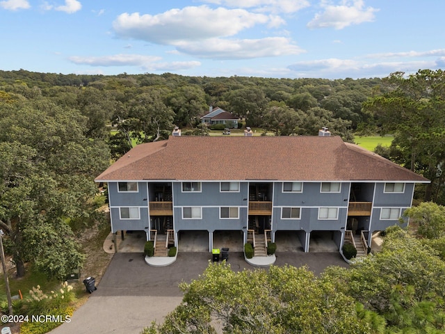 exterior space with a shingled roof, aphalt driveway, and a wooded view