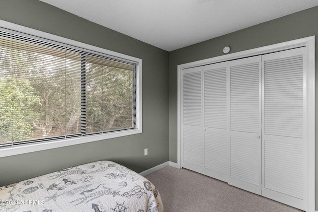 bedroom with baseboards, a closet, and light colored carpet